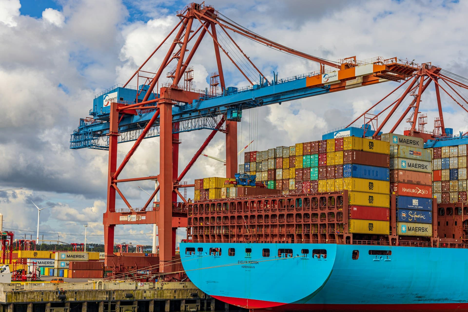 Blue-hulled container ship being loaded by red gantry cranes