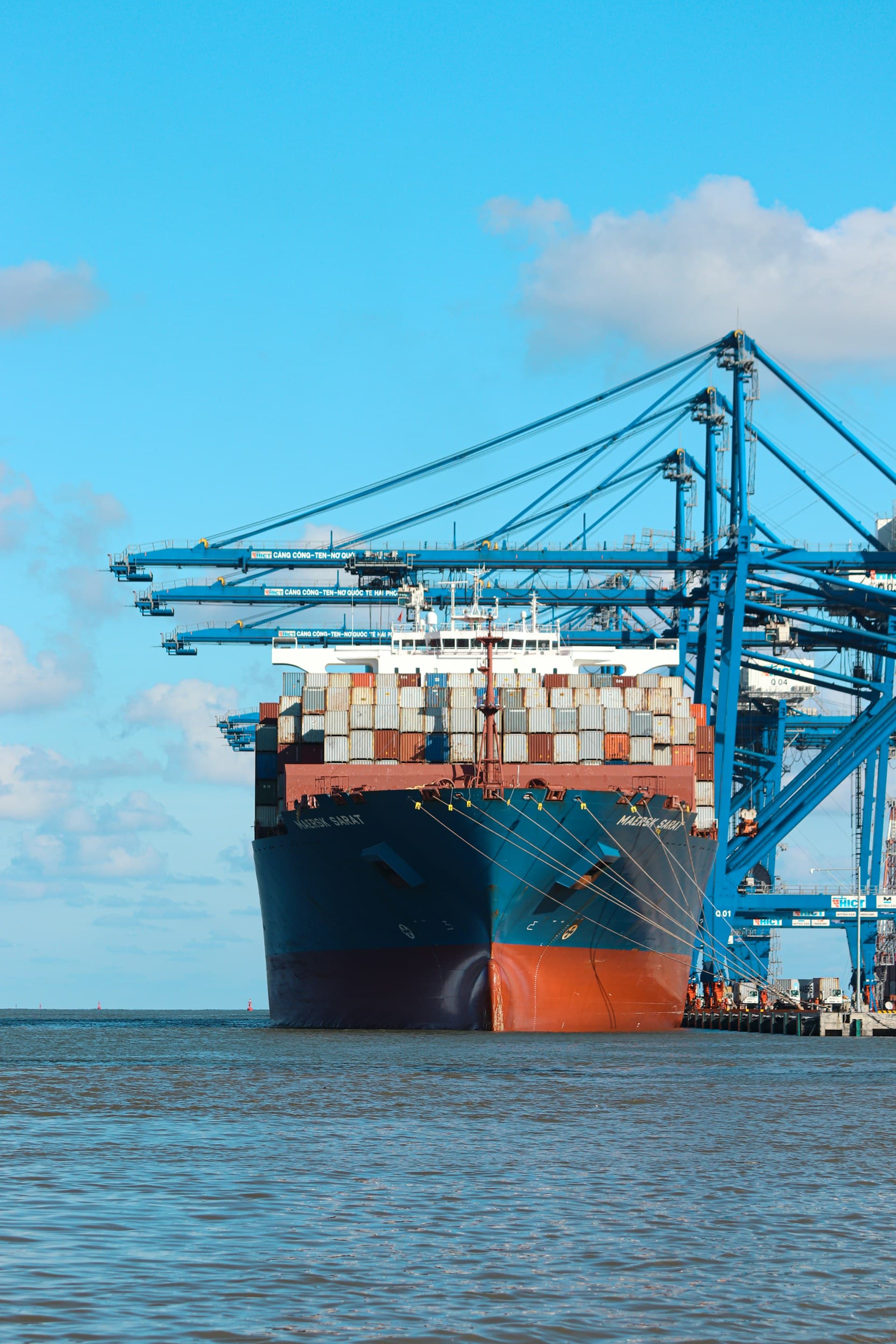 Container ship docked beside blue gantry cranes