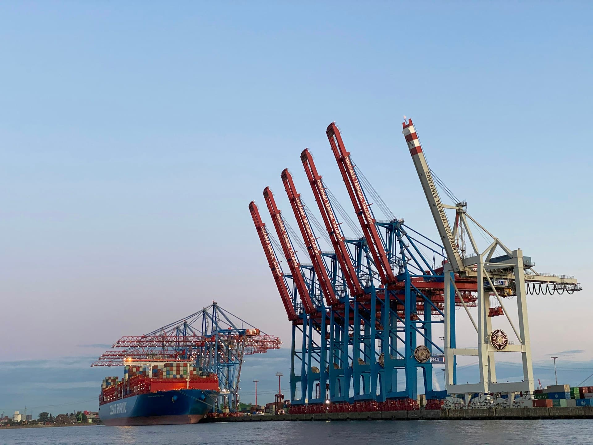 Silhouette of port cranes against a sunset sky