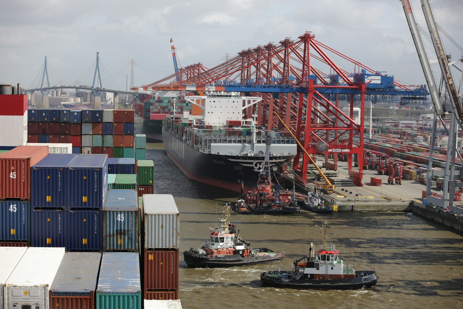 Tugboats guiding a container ship through a busy harbor